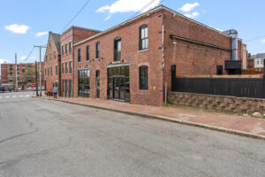 a red brick two story building in Portland, Maine that's viewed from the street with glass windows on both floors and a blue sky dotted with clouds above